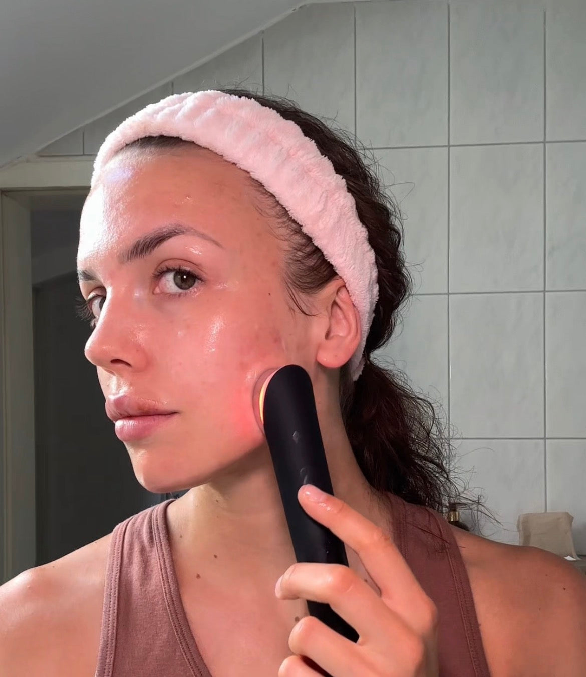 Frau mit Haarband nutzt das Skinqira Gerät mit rotem Licht im Badezimmer